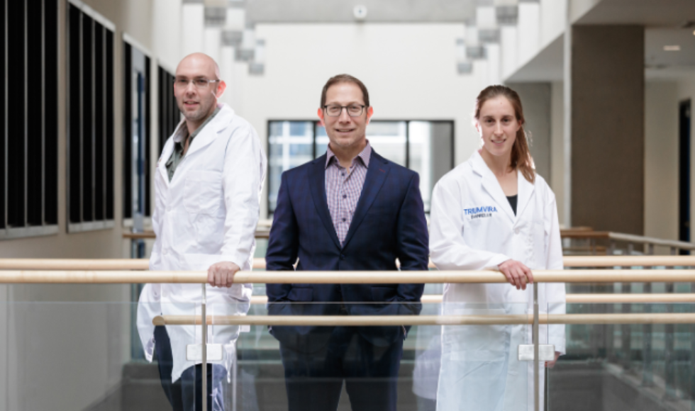 Three people in an atrium, two with lab coats and one in a suit