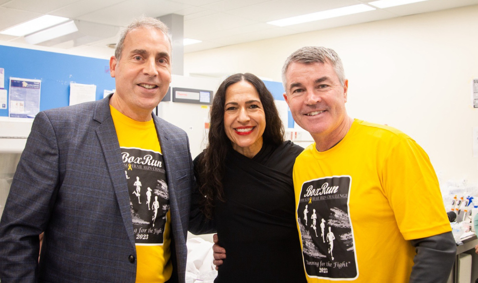 Three people smiling standing close together, two in yellow shirts and one in a black top