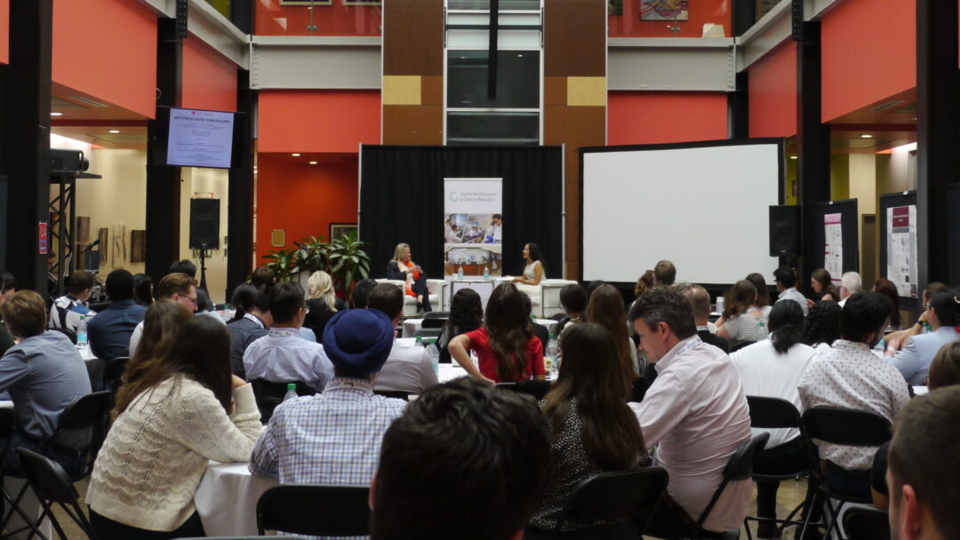 Crowd watching two people speak in white chairs on a stage