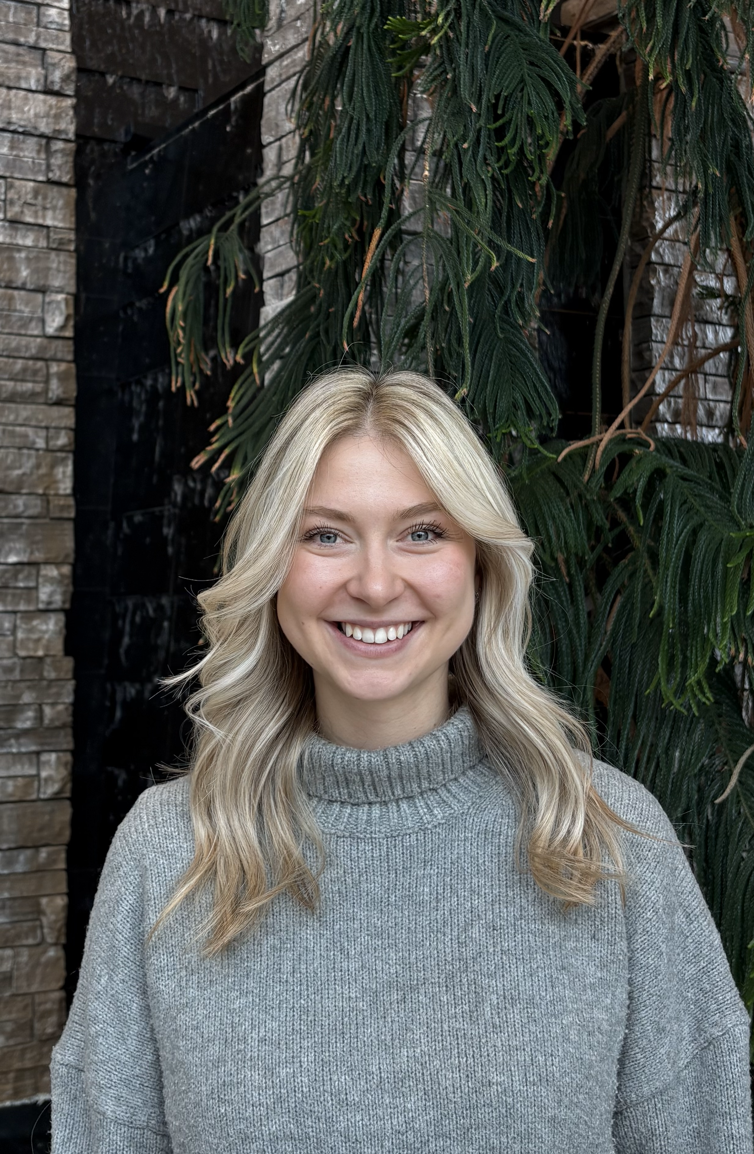 Person in grey sweater standing in front of tree